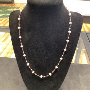 May include: A delicate necklace featuring a repeating pattern of small white pearls interspersed with tiny, faceted deep pink gemstone beads and small clear crystals, all connected by a thin metallic chain in a continuous, uniform design.