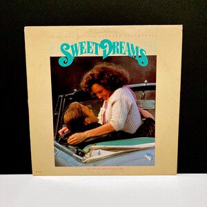 May include: A vintage vinyl record album cover for the "Sweet Dreams" soundtrack. The cover features a couple in a convertible car. The title is in turquoise script. The album is beige with the text "Original Motion Picture Soundtrack" at the top.