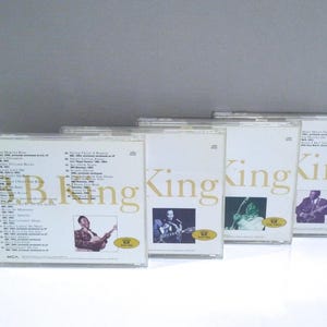 May include: A collection of B.B. King music CDs. The CD cases are clear with white and gold text. Each CD features a photo of B.B. King playing his guitar. The album titles are visible on the back of the CD cases.