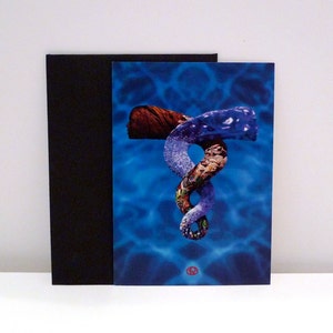 May include: A greeting card featuring an abstract design with a blue water background. The artwork includes a brown silhouette, a blue and white swirl, and a multi-colored section. A black card is behind the artwork.