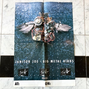 May include: A rectangular poster featuring a dark blue, textured metal background with a central mechanical bird sculpture made of electronic components and wires. The text reads JANITOR JOE BIG METAL BIRDS with three small band photos and blank AT: ON: fields.