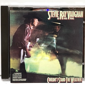 May include: CD case featuring Stevie Ray Vaughan and Double Trouble's album, "Couldn't Stand the Weather." The cover art shows a blurred image of a man playing a guitar. The CD case has the Compact Disc Digital Audio logo.