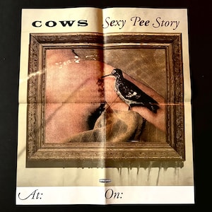 May include: A folded paper with the words "COWS" and "Sexy Pee Story" at the top. The image features a framed painting with a bird perched on a person's chest. The bottom of the paper has the words "At:" and "On:"