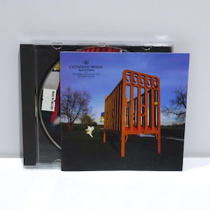 May include: A CD case with the album art for "Waydown" by Catherine Wheel. The cover art features an orange crib on a grassy field under a blue sky. The CD case is open, revealing the disc inside.