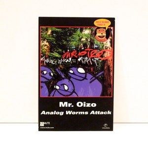 May include: A black CD case with the album title "Analog Worms Attack" by Mr. Oizo. The cover art features purple cartoon figures and forest imagery. The text "This is the music I dance to..." is also visible.