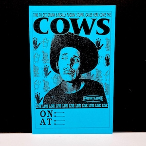 May include: A blue poster with black text and graphics. The poster features a black and white image of a man wearing a hat. Text includes "TIME TO GET DRUNK & REALLY FUGGIN' STUPID, CAUSE HERE COME THE COWS".