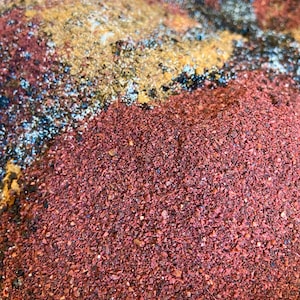May include: A close-up of a mixture of spices, including red, brown, and black. The spices are arranged in layers, creating a colourful and textured background.