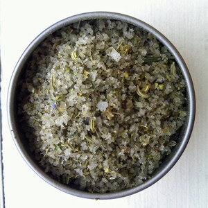 May include: A close-up of a metal container filled with a blend of salt and dried herbs. The salt is white and the herbs are a mix of green and brown.