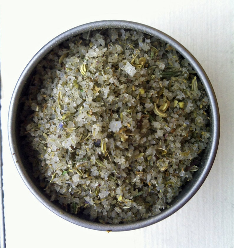 May include: A close-up of a metal container filled with a blend of salt and dried herbs. The salt is white and the herbs are a mix of green and brown.
