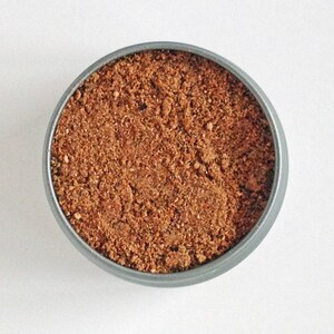 May include: A close-up of a small metal container filled with a brown spice blend.