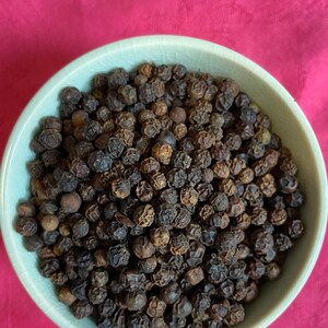 May include: A close-up view of a bowl filled with black peppercorns. The bowl is light green and the peppercorns are dark brown and black.