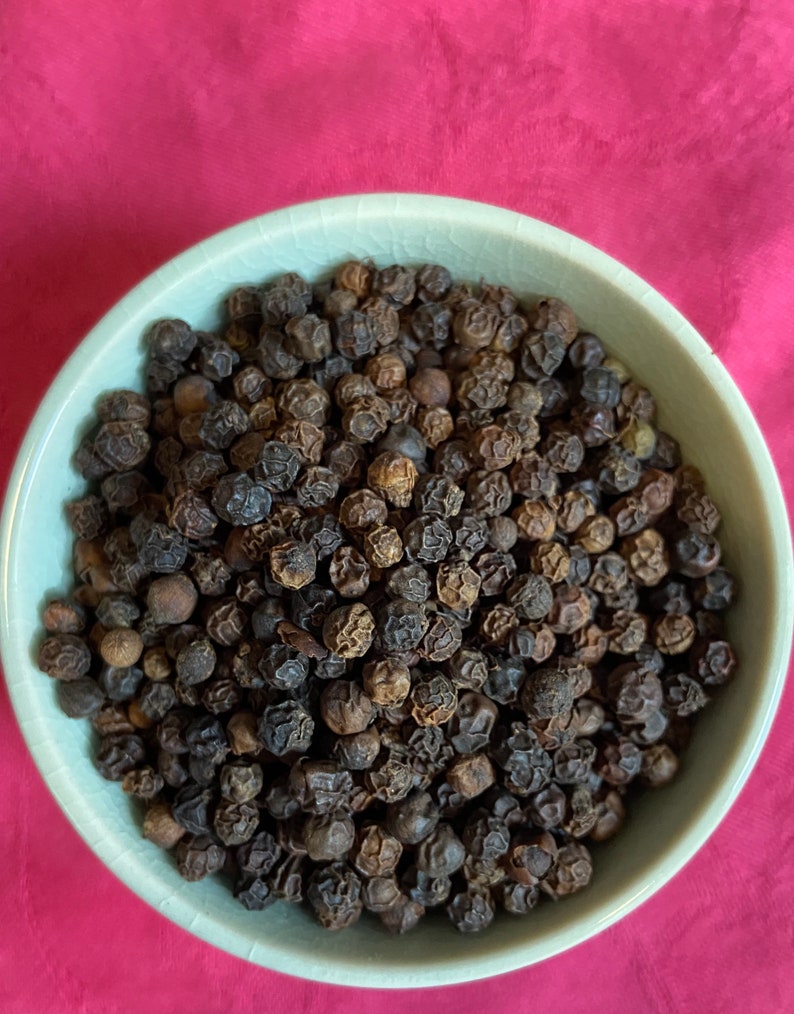 May include: A close-up view of a bowl filled with black peppercorns. The bowl is light green and the peppercorns are dark brown and black.