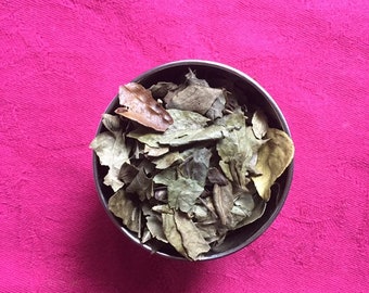 May include: A silver bowl filled with dried green and brown leaves. The bowl is sitting on a pink tablecloth.