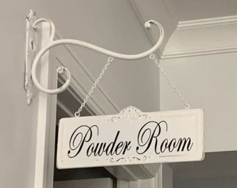 May include: White metal sign with black lettering that reads "Powder Room" hanging from a white metal hook.