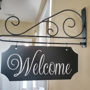 This is a custom metal hanging sign with a hanging rod and hanging hardware which are included. The sign is black with white writing. The writing is able to be perosnalized by you choosing your font and font color.