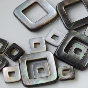 May include: A collection of black and iridescent mother of pearl square shaped pendants with a square hole in the center. The pendants are of varying sizes.