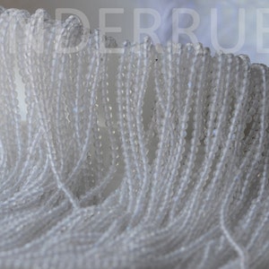 May include: A close-up of a pile of white round beads. The beads are small and have a smooth, polished finish.