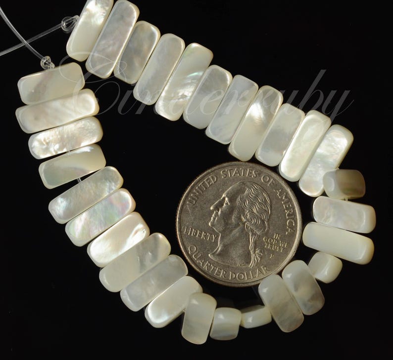 May include: A strand of rectangular, iridescent mother-of-pearl beads. A U.S. quarter coin is next to the beads for size comparison. The beads are strung on a thin, clear string against a black background. The beads have a pearly, opalescent sheen.