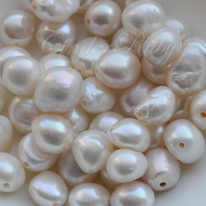 May include: A close-up of a group of white, pearlescent, irregular shaped pearls. The pearls are smooth and have a subtle iridescent sheen.