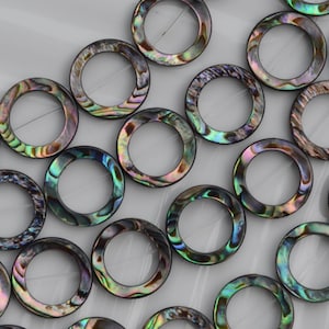 Könnte beinhalten: Eine Sammlung kreisförmiger Abalone-Muschelringe mit natürlichem irisierendem Finish und wirbelnden Mustern in Grün, Blau, Violett und Schwarz. Jeder Ring hat eine glatte, polierte Oberfläche und eine gleichmäßige, hohle Mitte.