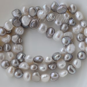May include: A strand of white and gray freshwater pearls. The pearls are irregular in shape and have a natural luster.