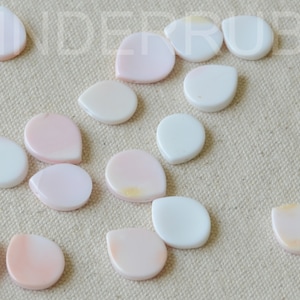 May include: A collection of 17 teardrop-shaped shell beads in white and pink. The beads are smooth and have a natural, iridescent sheen.
