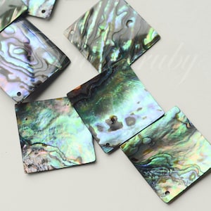 May include: A collection of iridescent square abalone shell beads. The beads display a range of colors, including green, blue, and silver, with a natural, textured pattern. Each bead has a small hole for stringing.