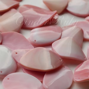 May include: A collection of pink, pearlescent shell shapes with a hole drilled through each one. The shells are smooth and have a natural, iridescent sheen.