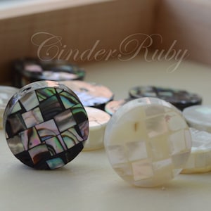 May include: Assortment of round, decorative buttons made from iridescent mother of pearl and abalone shell. The buttons feature a mosaic pattern of small squares in black, white, and iridescent colors.