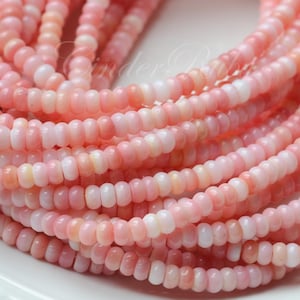 May include: A strand of pink and white shell beads. The beads are small and round, and they are strung together on a clear thread.
