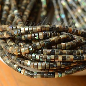 May include: A collection of multiple strands of small, flat, disc-shaped beads made from iridescent abalone shell. The beads feature a natural color palette of dark brown, tan, and grey tones with shimmering green and blue highlights throughout.