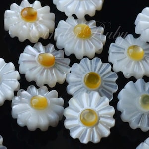 May include: A collection of white mother of pearl daisy flower cabochons with yellow centres. The cabochons are approximately 2.5 cm in diameter.
