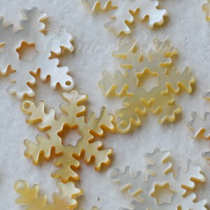 May include: A collection of white and gold snowflake-shaped ornaments made of mother of pearl. The ornaments have a delicate, intricate design.