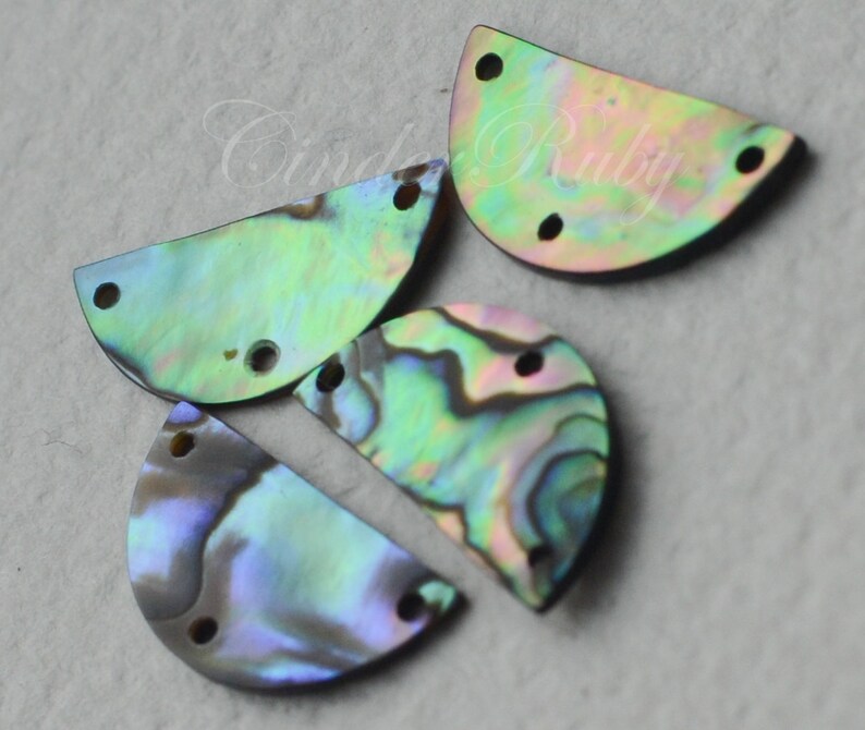 May include: Four iridescent abalone shell half-circles with two holes each. The shells are a mix of green, blue, and purple.