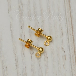 May include: Two gold-toned earring posts with a small ball at the end and a loop for attaching a charm or pendant.