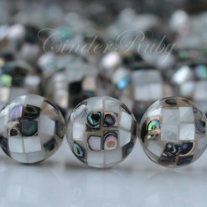 May include: A strand of round, iridescent beads made of white and black mosaic tiles. The beads have a subtle green and blue shimmer.