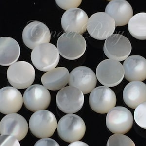 May include: A collection of white round iridescent shell cabochons. The cabochons are various sizes and have a smooth, polished surface.