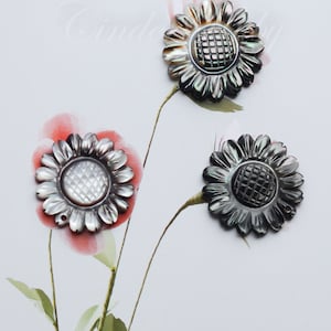 May include: Three black and iridescent mother of pearl sunflower shaped buttons with a grid pattern in the center.
