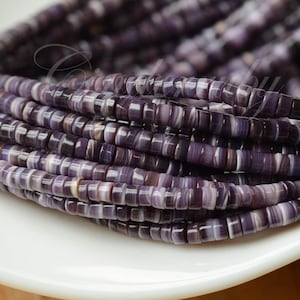 May include: A strand of small, flat, disc-shaped beads in varying shades of deep purple and white. The beads are arranged in a tight, coiled formation, showcasing a smooth, polished finish with distinct horizontal banding patterns on each individual bead.