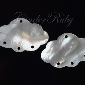 May include: Two white iridescent shell cloud-shaped embellishments with four holes each.