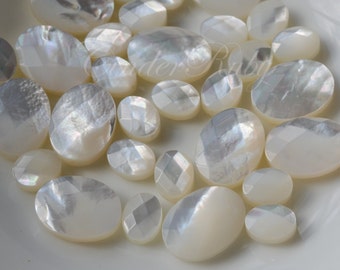 May include: A collection of white oval-shaped mother of pearl cabochons. The cabochons have a smooth, polished surface and a slightly iridescent sheen.