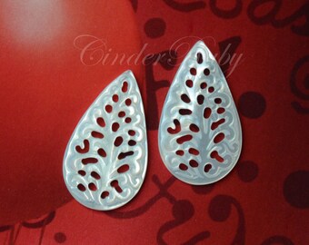 May include: Two white mother of pearl teardrop shaped pendants with a carved leaf design.