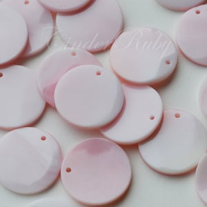 May include: A collection of pink, round, iridescent sequins with a hole in the center. The sequins are scattered on a white surface.