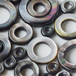 May include: A collection of black and iridescent mother of pearl shell beads with different sized holes. The beads are round and have a smooth, polished finish.