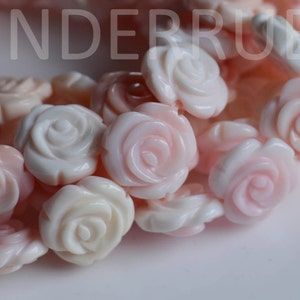 May include: A strand of pink and white carved coral rose beads. The beads are all in the shape of a rose and have a delicate, feminine look.