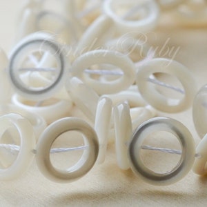 May include: A strand of white shell beads with a hole in the center of each bead. The beads have a subtle gray ring around the hole.