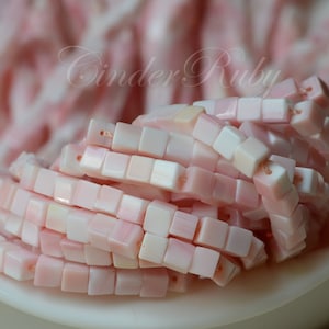 May include: A strand of pink and white square-shaped shell beads. The beads are made of natural shell and have a smooth, polished finish.