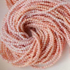 May include: Close-up of a pile of light pink beads. The beads are small, round, and strung together, creating a textured, swirling pattern. The color is a soft, muted pink, with variations in tone. Ideal for jewelry making.