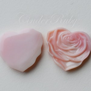May include: Two pink heart-shaped shell carvings. One is a simple heart shape, the other is carved with a rose design.