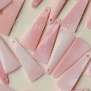 May include: A collection of pale pink, triangular pendants with a hole at the top for stringing. The pendants vary in shade from a soft white to a deeper pink. The pendants are likely for jewelry making.